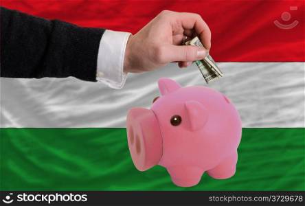 Man putting dollar into piggy rich bank national flag of hungary in foreign currency because of inflation