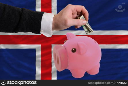 Man putting dollar into piggy rich bank national flag of iceland in foreign currency because of inflation