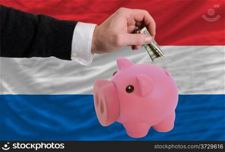 Man putting dollar into piggy rich bank national flag of netherlands in foreign currency because of inflation