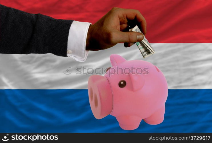 Man putting dollar into piggy rich bank national flag of netherlands in foreign currency because of inflation