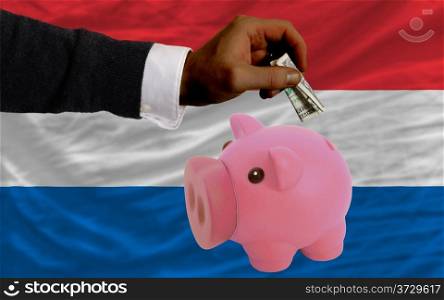 Man putting dollar into piggy rich bank national flag of netherlands in foreign currency because of inflation