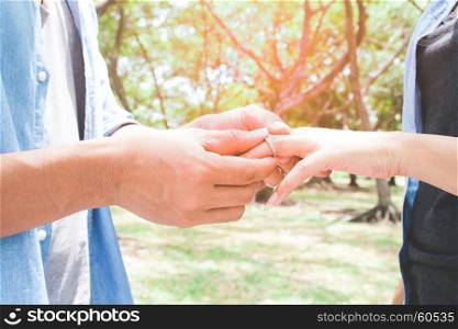 Man putting engagement silver ring on woman hand, outdoor, Green garden with bokeh