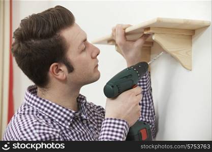 Man Putting Up Wooden Shelf At Home Using Electric Cordless Drill