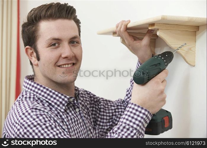 Man Putting Up Wooden Shelf At Home Using Electric Drill