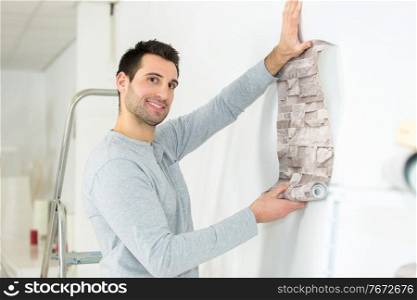 man putting wall paper against the wall