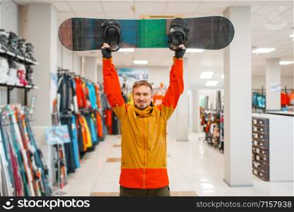 Man raised up the board for snowboarding, shopping in sports shop. Winter season extreme lifestyle, active leisure store, customer buying skiing equipment