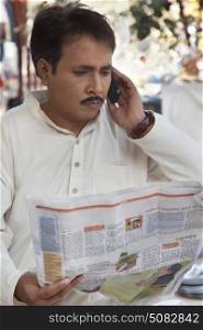 Man reading a newspaper and talking on a mobile phone