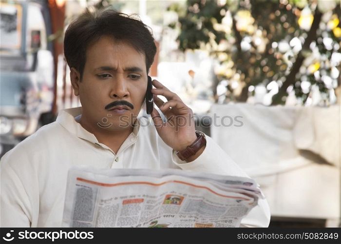 Man reading a newspaper and talking on a mobile phone