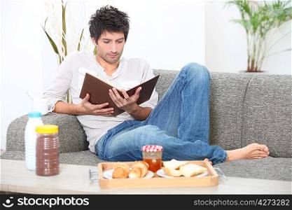 Man reading and having breakfast on a sofa