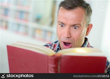 Man reading book, horrified expression
