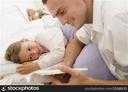 Man reading book to young girl in bed smiling
