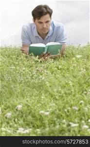 Man reading book while lying on grass against sky