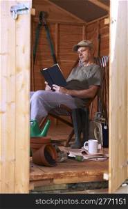 Man reading book while sitting in deckchair in his garden shed