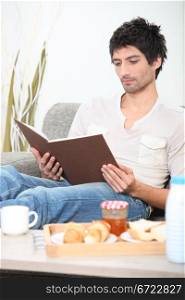 Man reading book whilst eating breakfast