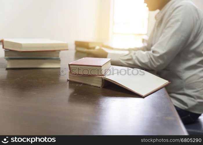 man reading book with textbook stack on wooden desk in library