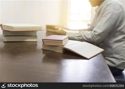 man reading book with textbook stack on wooden desk in library