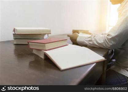 man reading book with textbook stack on wooden desk in library