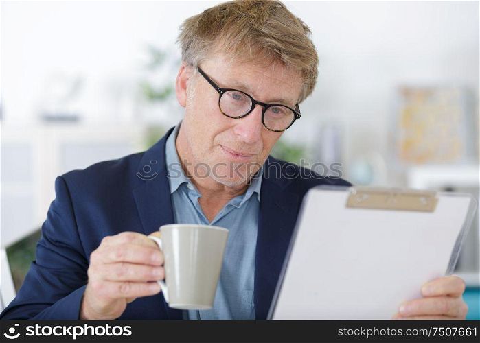 man reading clipboard with coffee mug on table