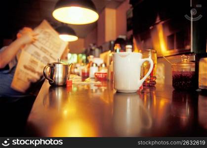 Man reading newspaper by bar counter with coffee cup in foreground