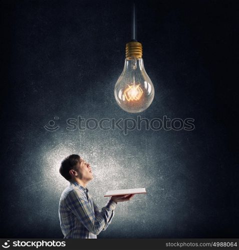 Man reading red book. Young student guy with opened book in hands and glass light bulb