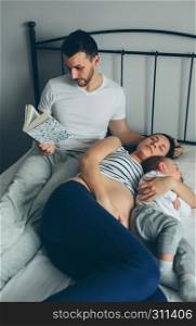 Man reading while his pregnant wife and son are sleeping. Man reading with pregnant wife and son sleeping