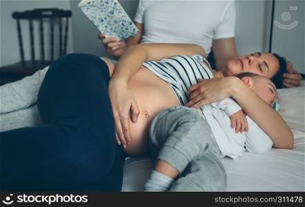 Man reading while his pregnant wife and son are sleeping. Man reading with pregnant wife and son sleeping