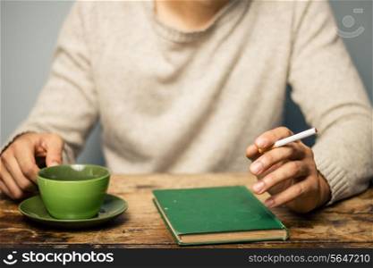 Man reading whilst smoking cigarette and having coffee
