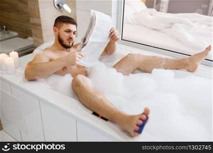 Man reads newspaper in bath with foam, morning hygiene. Male person relax in bathroom, skin and body treatments procedures. Man reads newspaper in bath with foam