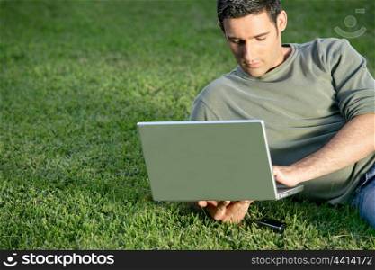 Man relaxing in field with laptop