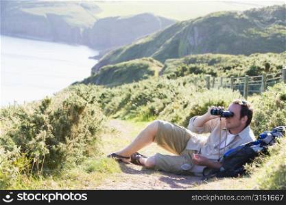 Man relaxing on cliffside path using binoculars
