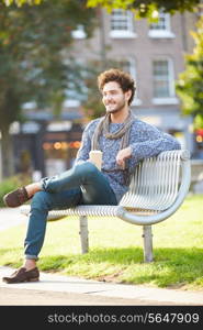 Man Relaxing On Park Bench With Takeaway Coffee