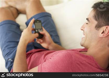 Man Relaxing On Sofa Sending Text Message