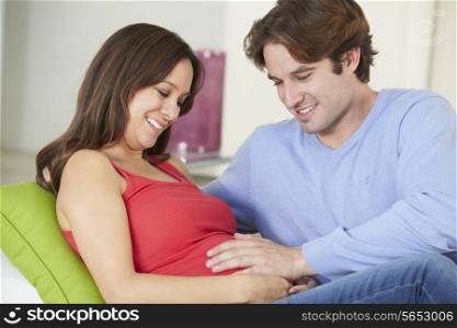 Man Relaxing On Sofa With Pregnant Wife At Home