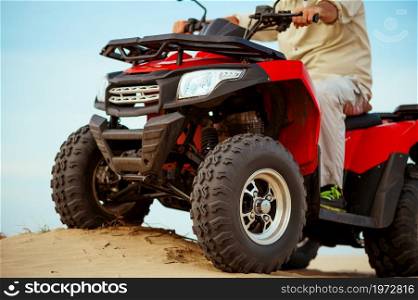 Man rides on atv, downhill riding in desert sands, action view. Male person on quad bike, sandy race, dune safari in hot sunny day, 4x4 extreme adventure, quad-biking. Man in helmet rides on atv in desert, action view