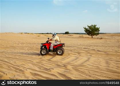 Man rides on atv in desert sands. Male person on quad bike, sandy race, dune safari in hot sunny day, 4x4 extreme adventure, quad-biking. Man in helmet rides on atv in desert sands