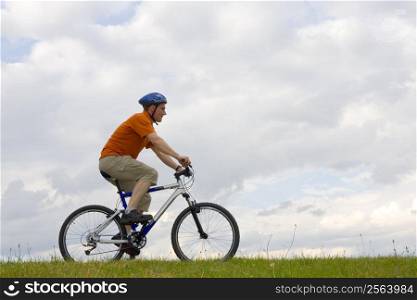 Man riding a mountain bike in a meadow against cloudy sky