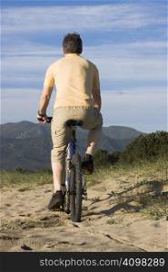 Man riding bicycle on the beach with hills in the background
