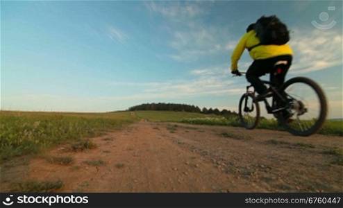 Man riding bicycle through a field in the morning. Rear view, wide-angle lens.