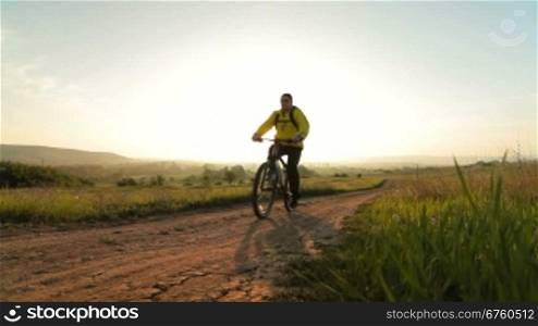 Man riding bicycle through the morning field at sunrise