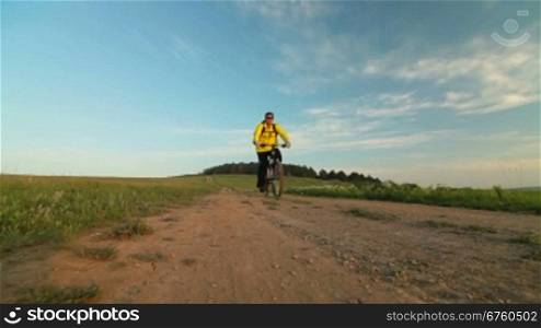 Man riding bike down a country lane through a field