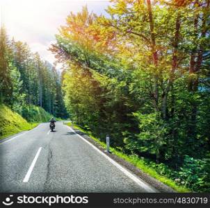 Man riding on motorbike on mountainous highway along beautiful fresh forest in bright sunny day, traveling in Europe, journey and freedom concept