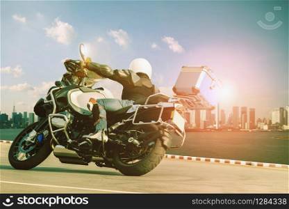 man riding touring motorcycle on sharp curve for traveling and city lifestyle. man riding touring motorcycle on sharp curve against sunset sky and high building in town skyscraper