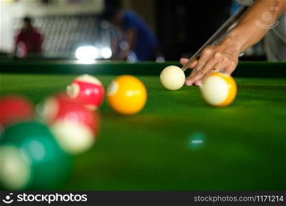 Man&rsquo;s hand and Cue arm playing snooker game or preparing aiming to shoot pool balls on a green billiard table. Colorful snooker balls on green frieze