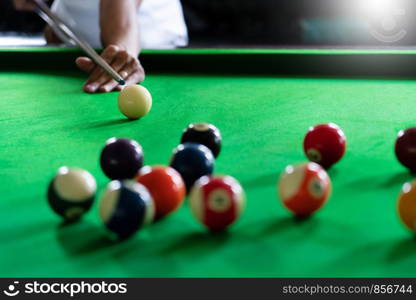 Man's hand and Cue arm playing snooker game or preparing aiming to shoot pool balls on a green billiard table