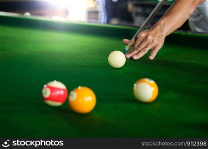 Man's hand and Cue arm playing snooker game or preparing aiming to shoot pool balls on a green billiard table. Colorful snooker balls on green frieze