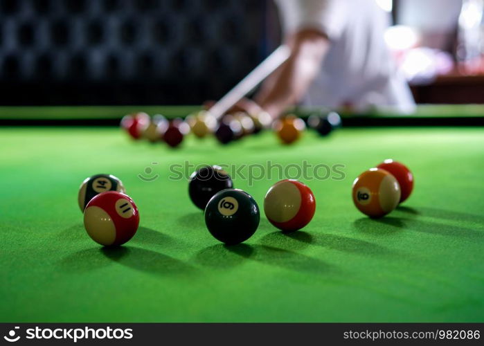 Man's hand and Cue arm playing snooker game or preparing aiming to shoot pool balls on a green billiard table. Colorful snooker balls on green frieze