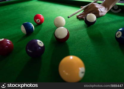 Man's hand and Cue arm playing snooker game or preparing aiming to shoot pool balls on a green billiard table