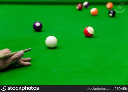 Man's hand and Cue arm playing snooker game or preparing aiming to shoot pool balls on a green billiard table