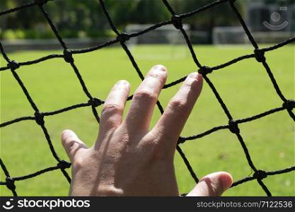 Man&rsquo;s hand extended to touch the mesh of a football field.