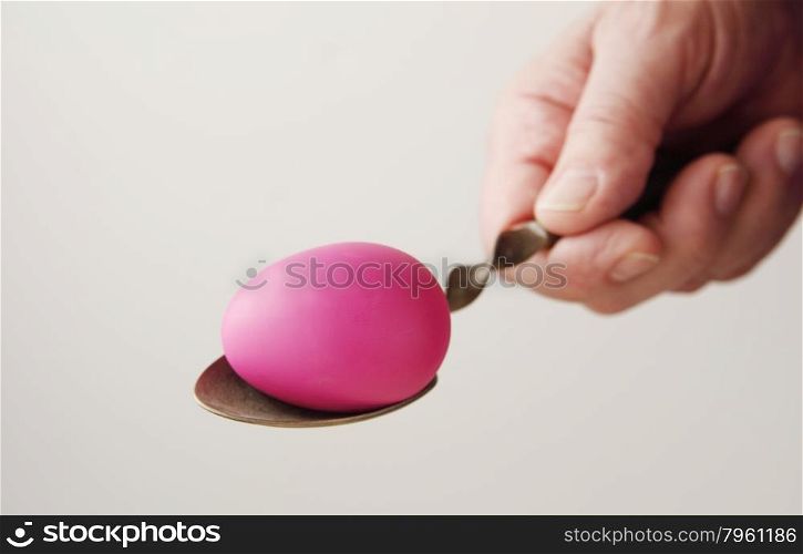 man&rsquo;s hand holding an ornate old spoon with a deep pink Easter egg